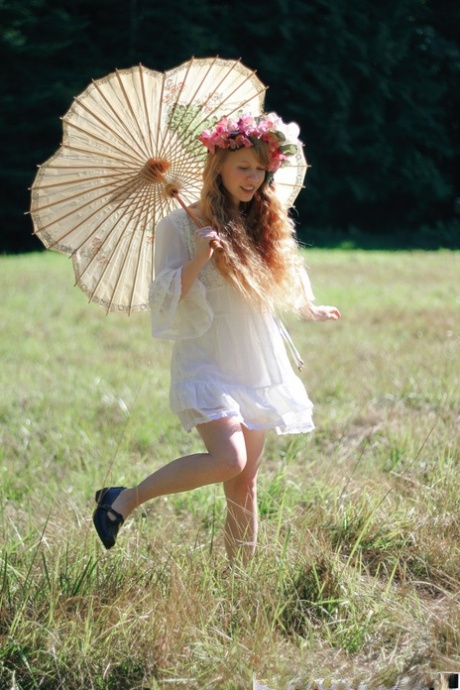 Charming redheaded teen Dolly Little holds a parasol while getting naked