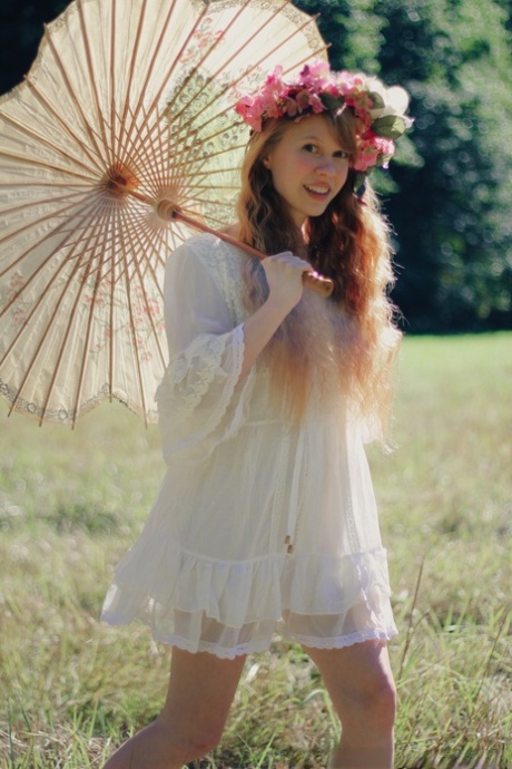 Charming redheaded teen Dolly Little holds a parasol while getting naked