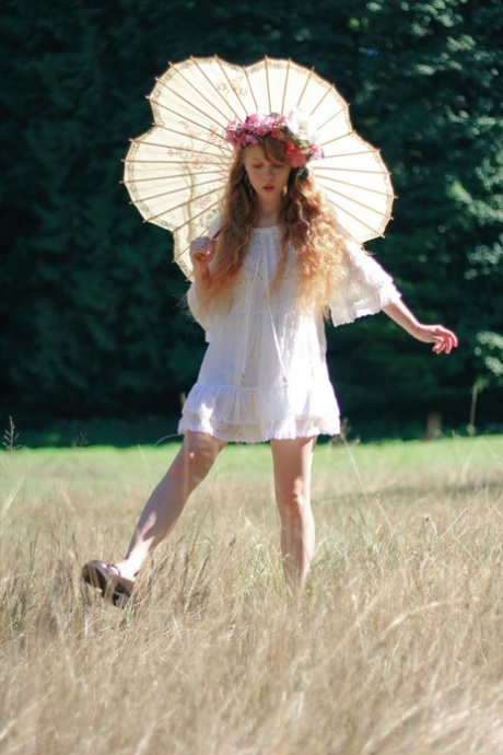 Charming redheaded teen Dolly Little holds a parasol while getting naked