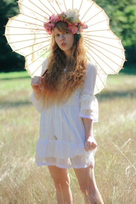 Charming redheaded teen Dolly Little holds a parasol while getting naked