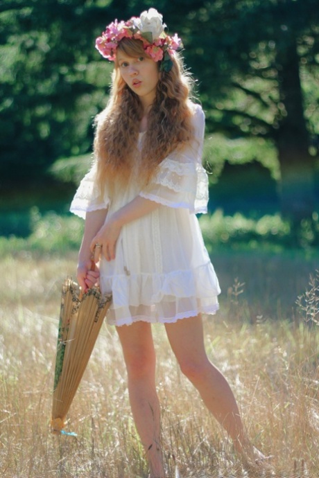 Charming redheaded teen Dolly Little holds a parasol while getting naked