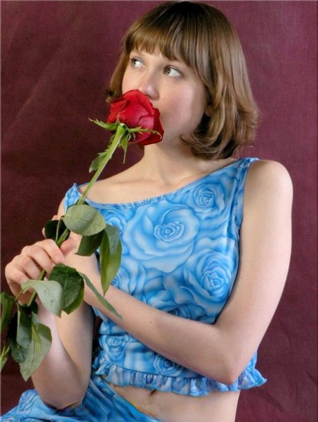 Charming teen Anabell holds a solitary red rose while taking off her clothes