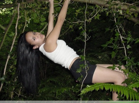 Pretty Indian girl hangs from a tree limb in a tank top and shorts