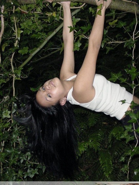 Pretty Indian girl hangs from a tree limb in a tank top and shorts