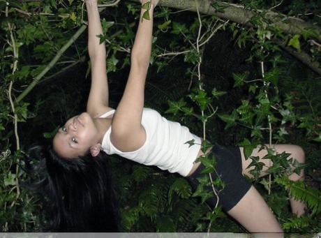 Pretty Indian girl hangs from a tree limb in a tank top and shorts