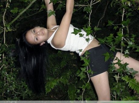 Pretty Indian girl hangs from a tree limb in a tank top and shorts