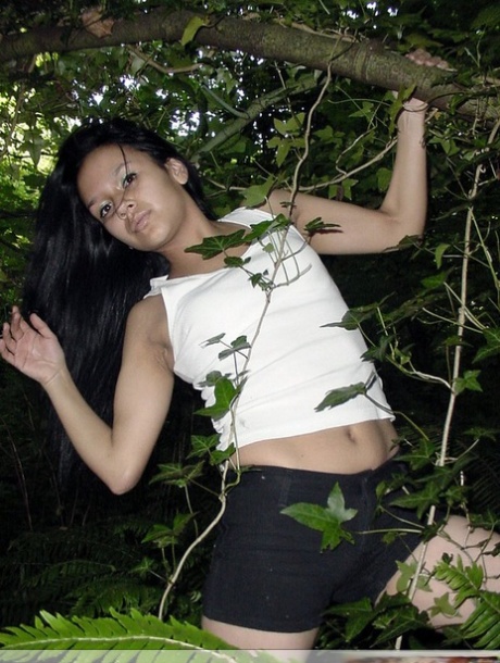 Pretty Indian girl hangs from a tree limb in a tank top and shorts