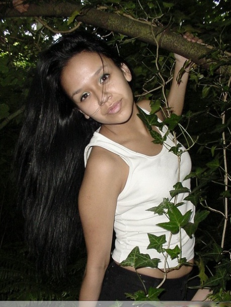 Pretty Indian girl hangs from a tree limb in a tank top and shorts