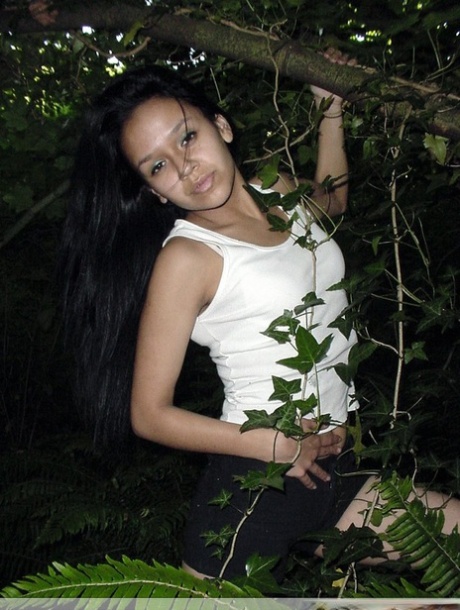 Pretty Indian girl hangs from a tree limb in a tank top and shorts