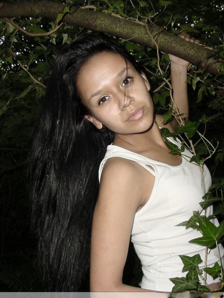 Pretty Indian girl hangs from a tree limb in a tank top and shorts