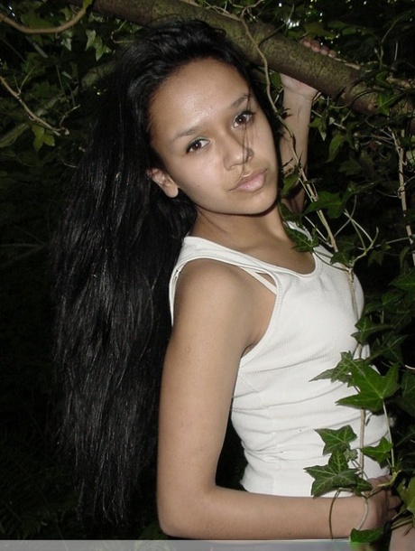 Pretty Indian girl hangs from a tree limb in a tank top and shorts