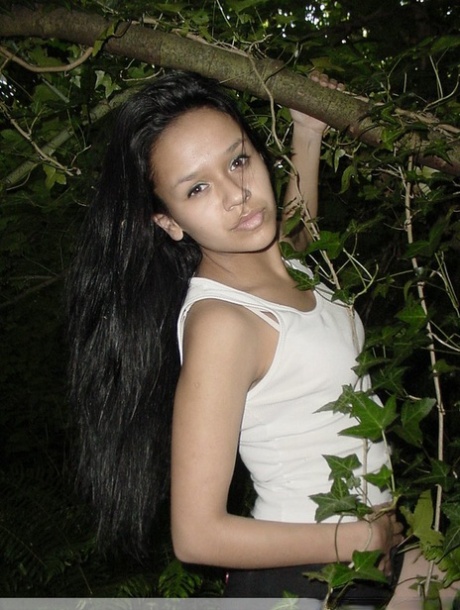 Pretty Indian girl hangs from a tree limb in a tank top and shorts