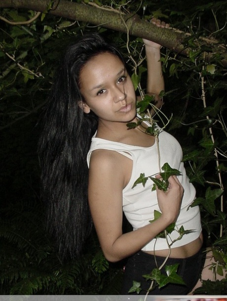 Pretty Indian girl hangs from a tree limb in a tank top and shorts