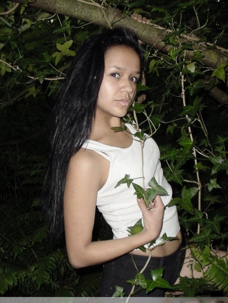 Pretty Indian girl hangs from a tree limb in a tank top and shorts