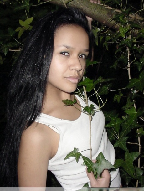 Pretty Indian girl hangs from a tree limb in a tank top and shorts