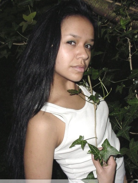 Pretty Indian girl hangs from a tree limb in a tank top and shorts
