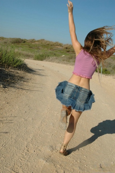 Young girl frolics on a dirt road well wearing a denim miniskirt and a thong