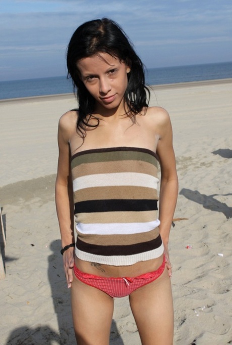 Thin brunette holds her bare ass while barefoot on a sandy beach