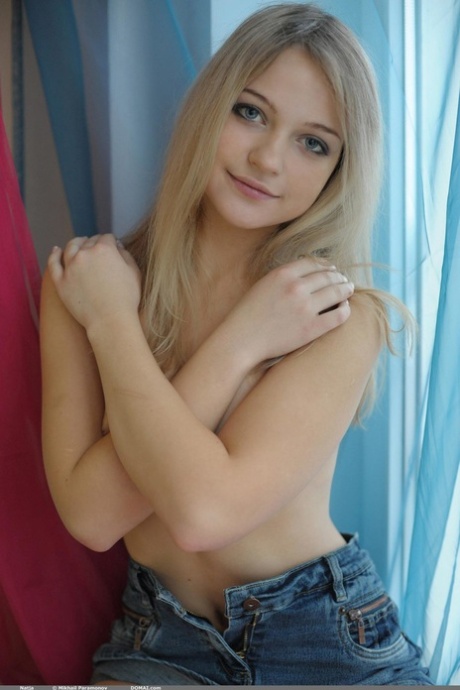 Sweet blonde teen Natja gets naked by a window in a casual manner