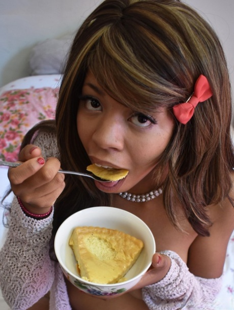 Black babe in gray socks Little Yumi flaunts her tits while eating on a bed