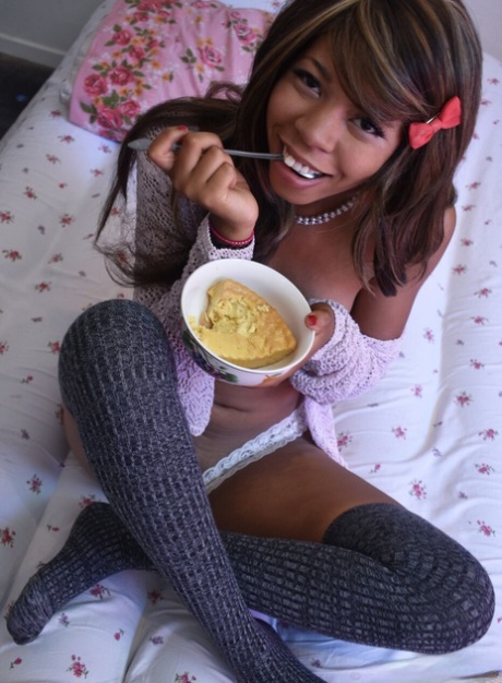 Black babe in gray socks Little Yumi flaunts her tits while eating on a bed