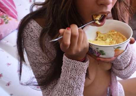 Black babe in gray socks Little Yumi flaunts her tits while eating on a bed