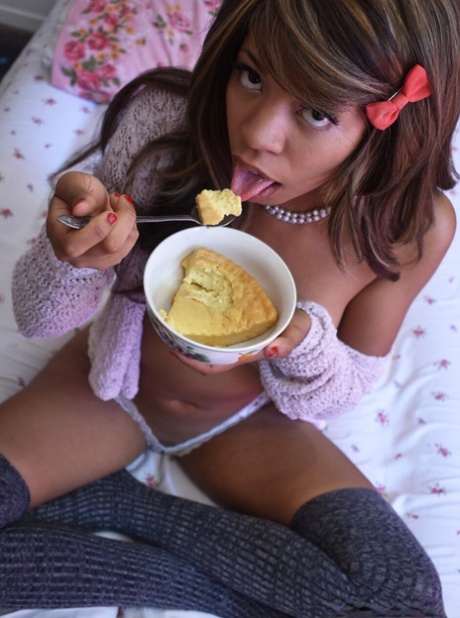 Black babe in gray socks Little Yumi flaunts her tits while eating on a bed